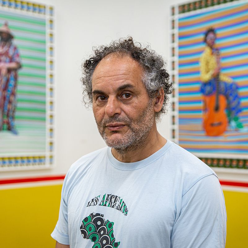 Hassan Hajjaj closeup portrait photo with two of his artworks blurred behind him