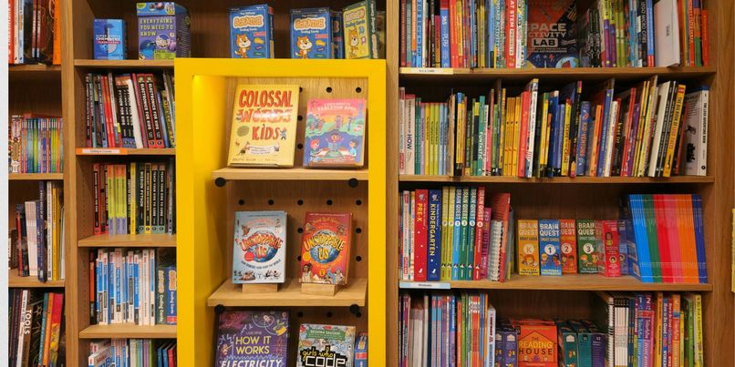 Bookshelves filled with colorful children's books, educational books, and activity kits, with a yellow display section in the center.