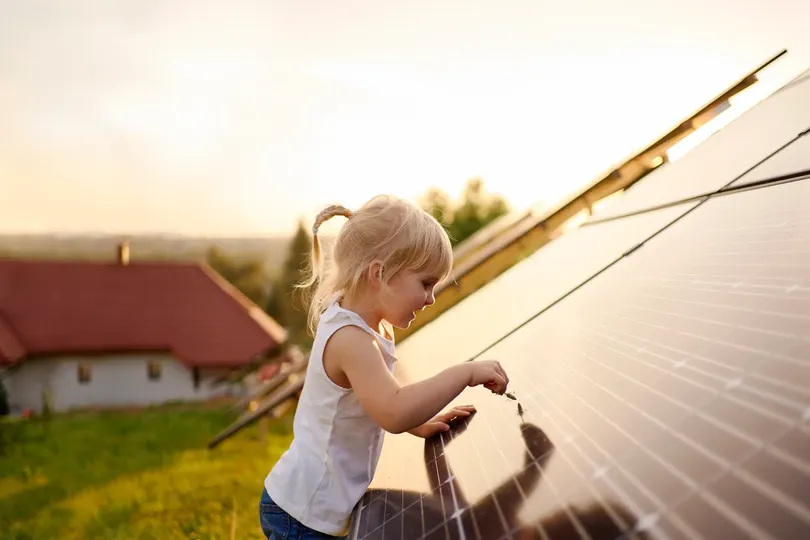 young girl touching a piece of grass to a solar panel in the back garden