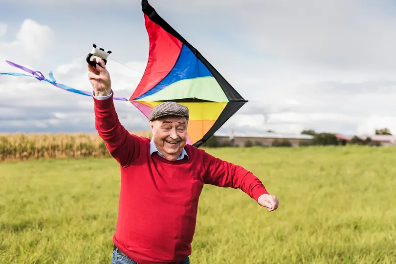 senior man happily flying kite in field