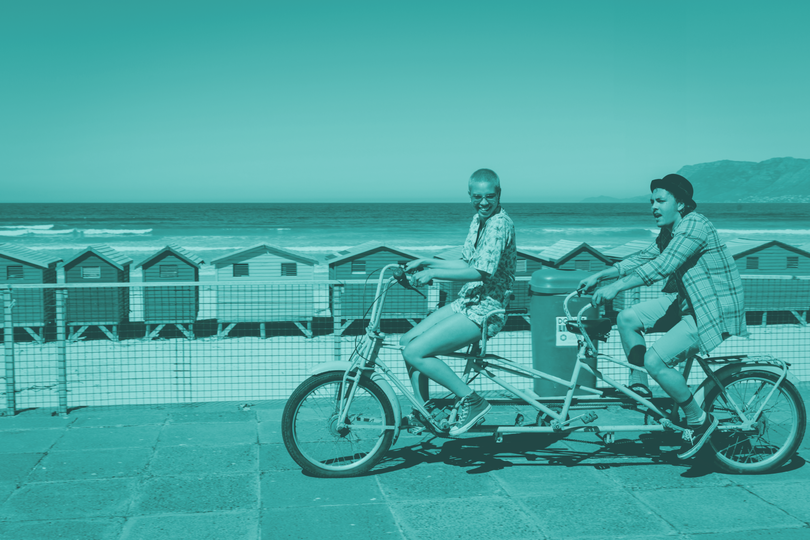 two people cycling along the seafront promenade on a tandem bicycle