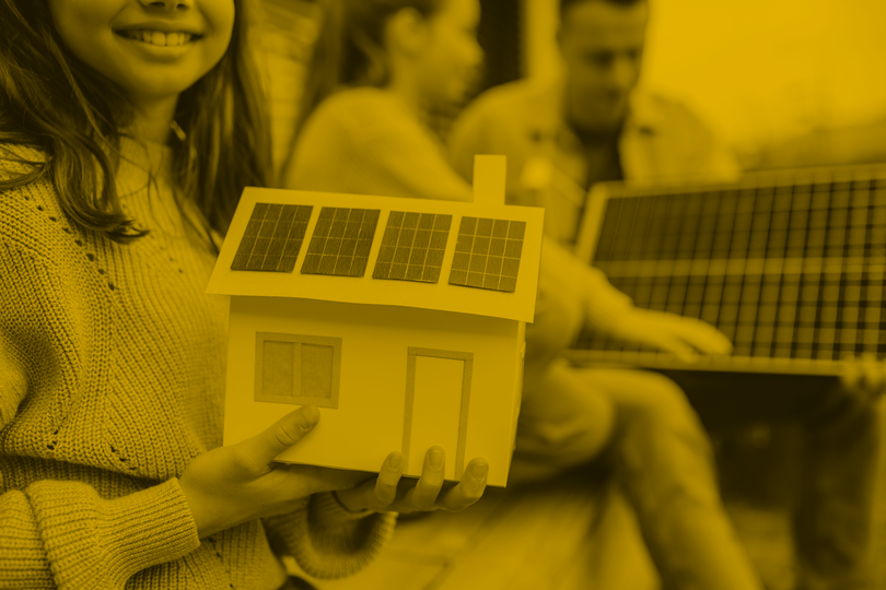Cheerful girl holding model of house with solar panels, father explaining her sister how it works. Alternative energy, saving resources and sustainable lifestyle concept.