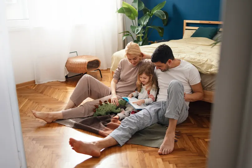 family happily sitting on floor in sleepwear reading book