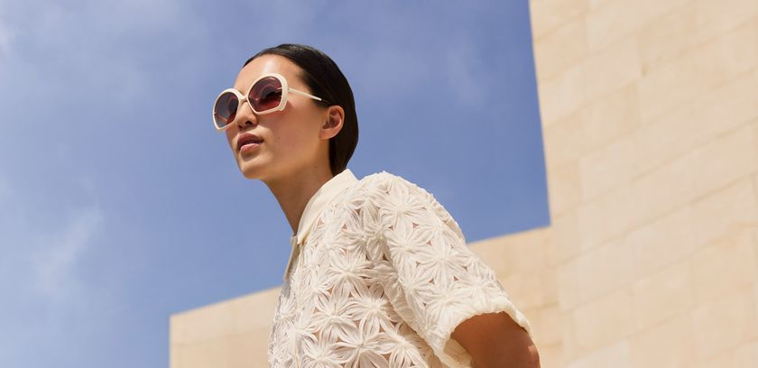 Woman wearing round Silhouette sunglasses with a light frame against a blue background.