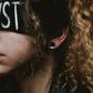 A woman wears a blindfold with 'Trust' written on the front
