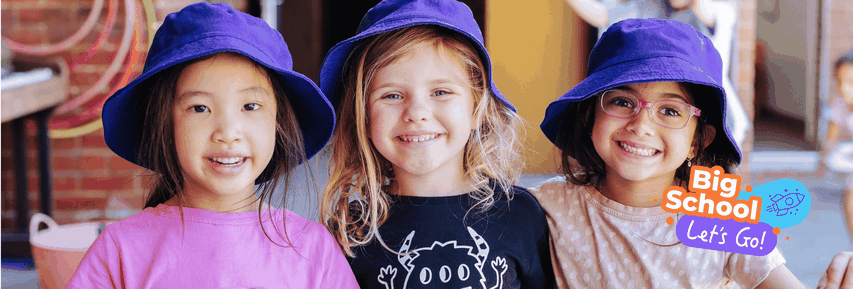 Three smiling young girls wearing purple hats, standing close together. A graphic reads "Big School, Let's Go!" with a rocket illustration.