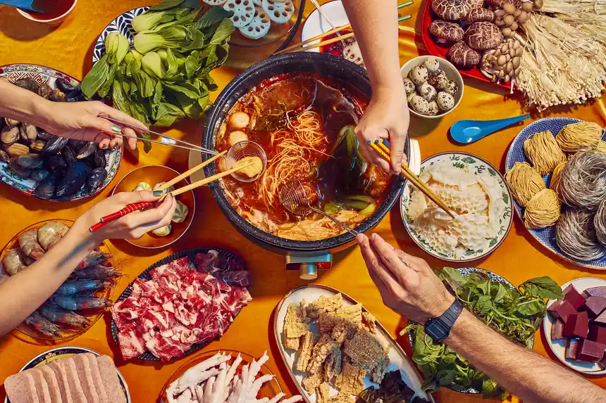 An overhead view of the hot pot with food cooking in it and next to it on the table, people dipping food into it
