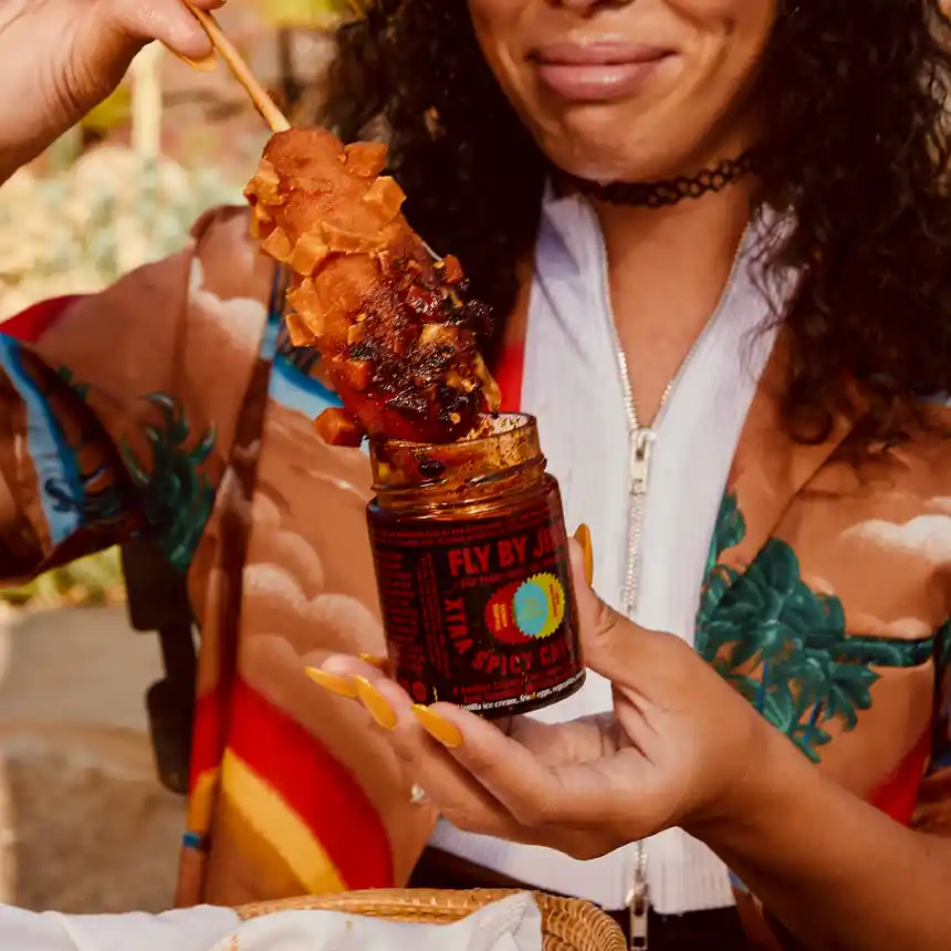 A woman dipping corn into a jar of Xtra Spicy Chili Crisp