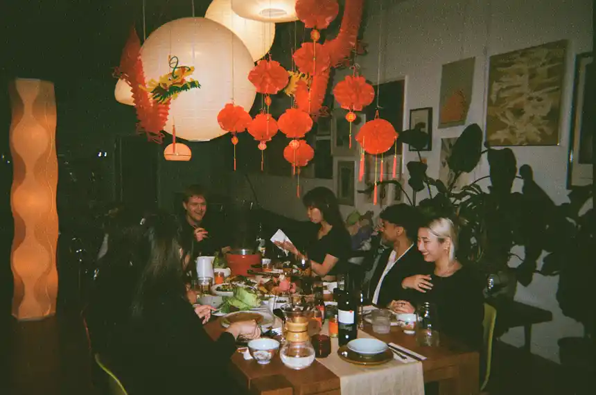 several people gathered around a table under festive decor for a lunar new year dinner party