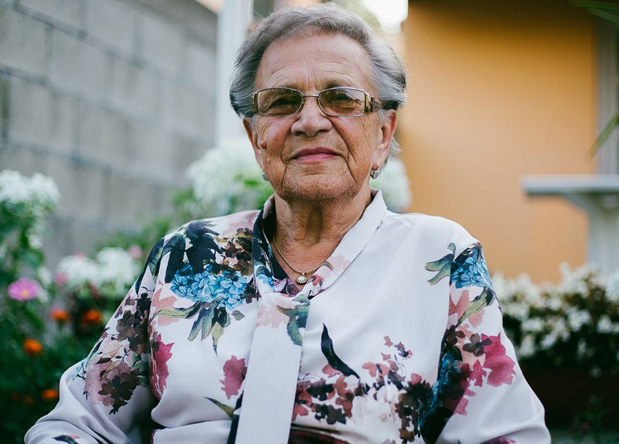 Photo of an older lady with grey hair and glasses, sitting in her garden wearing a floral shirt while doing an aged care ACAT assessment