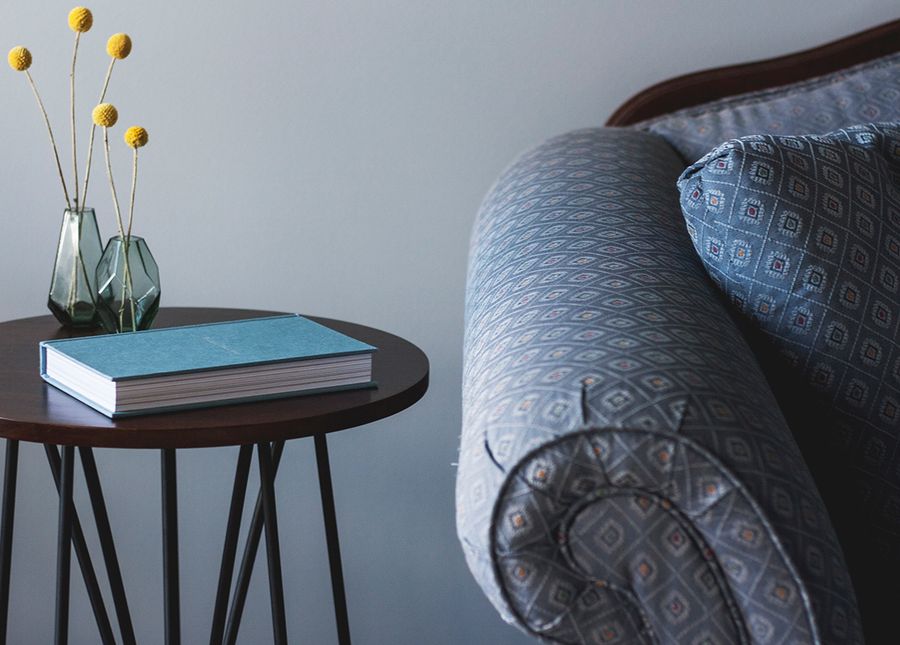 Photo of a veteran's room in residential aged care showing a blue lounge, round brown table with a blue book and yellow flowers in a vase on it