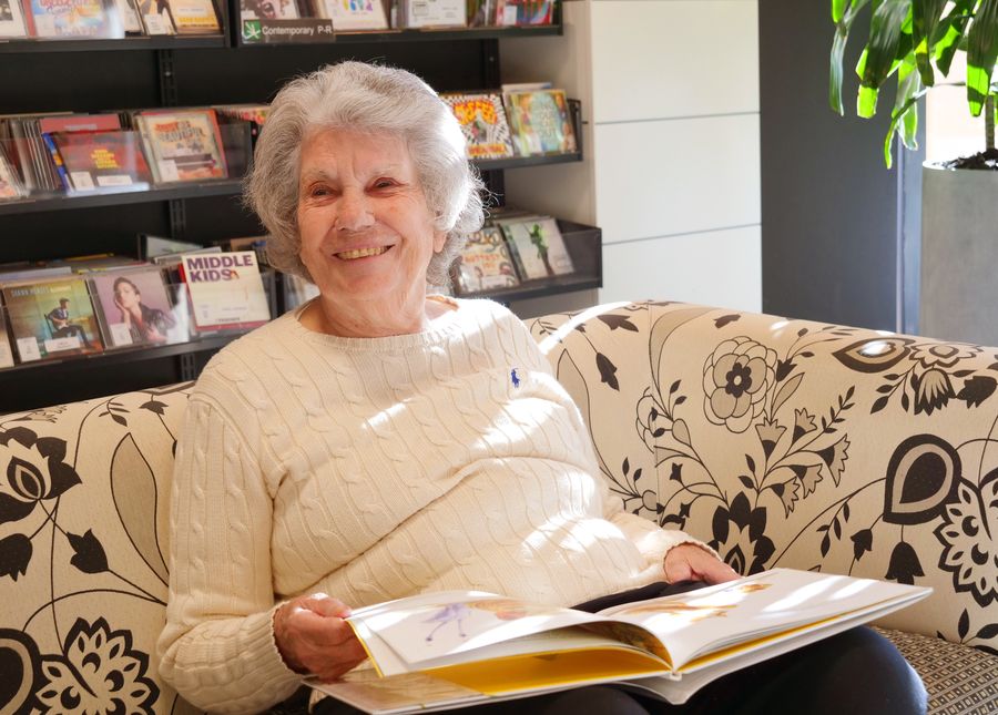 Travelling with dementia- Older lady sitting on a lounge with an open book smiling