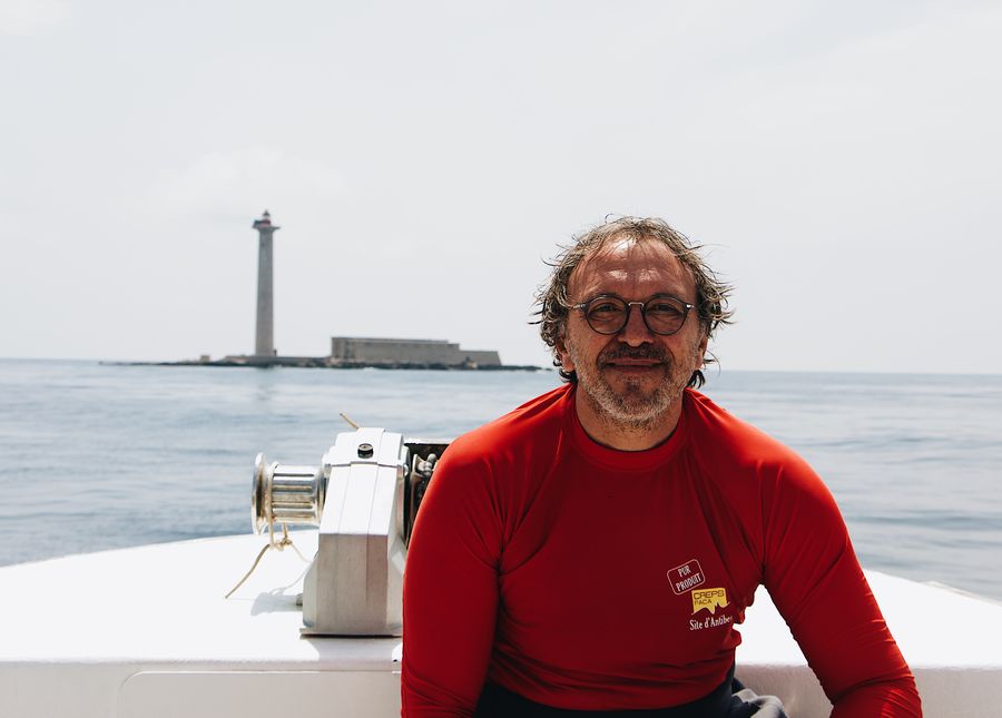 residential aged care fees- photo of an older man in a red rash vest on a boat smiling at the camera. There is a lighthouse in the background