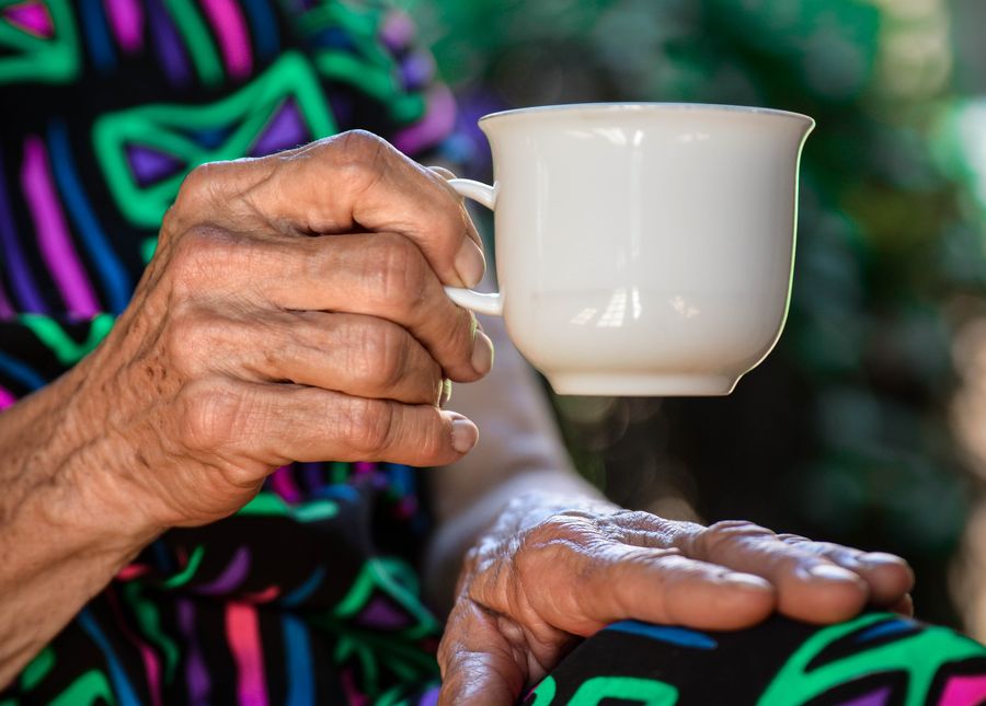 Close up photo of an aged care visitors hands holding a white cup of tea