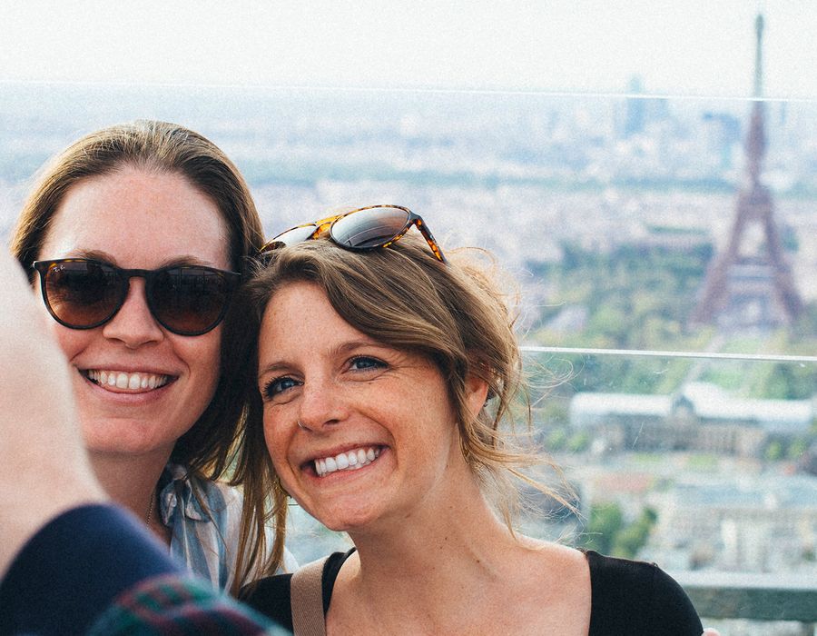 two women taking a selfie with the Eiffel tower in the background in France