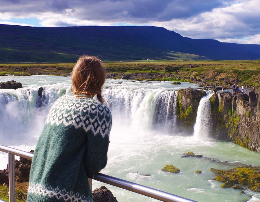 woman looking out at godafoss waterfall in iceland on a sunny day