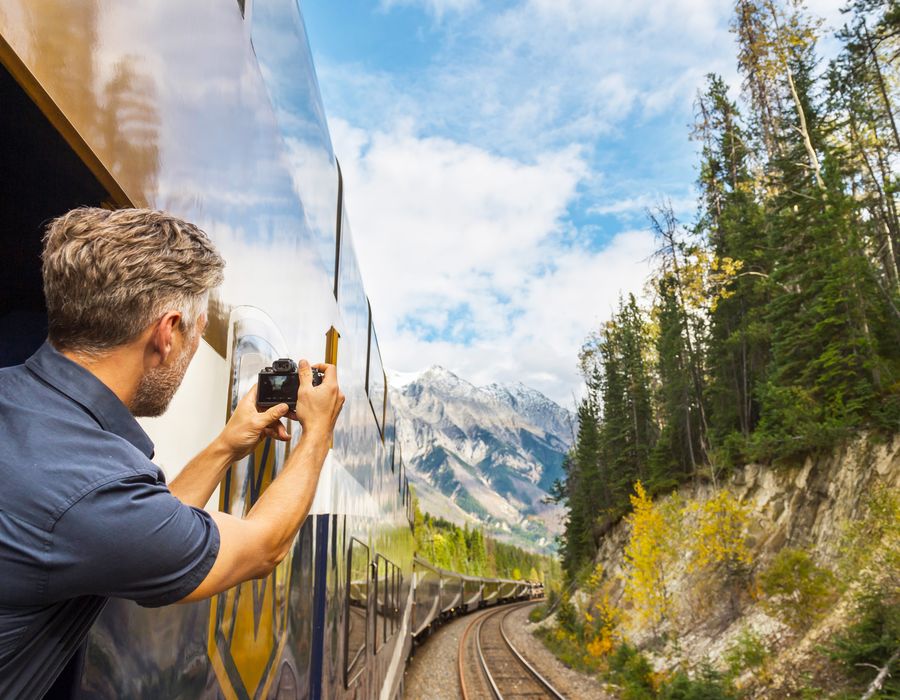 man looking out window of a train taking a photo of the swiss alps