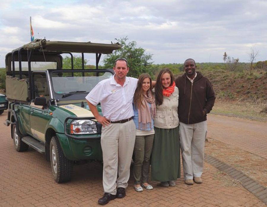 two group travelers with staff members with safari truck behind them