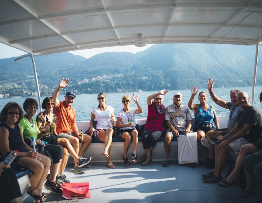 group of travelers waving at the camera from a boat on lake como in italy