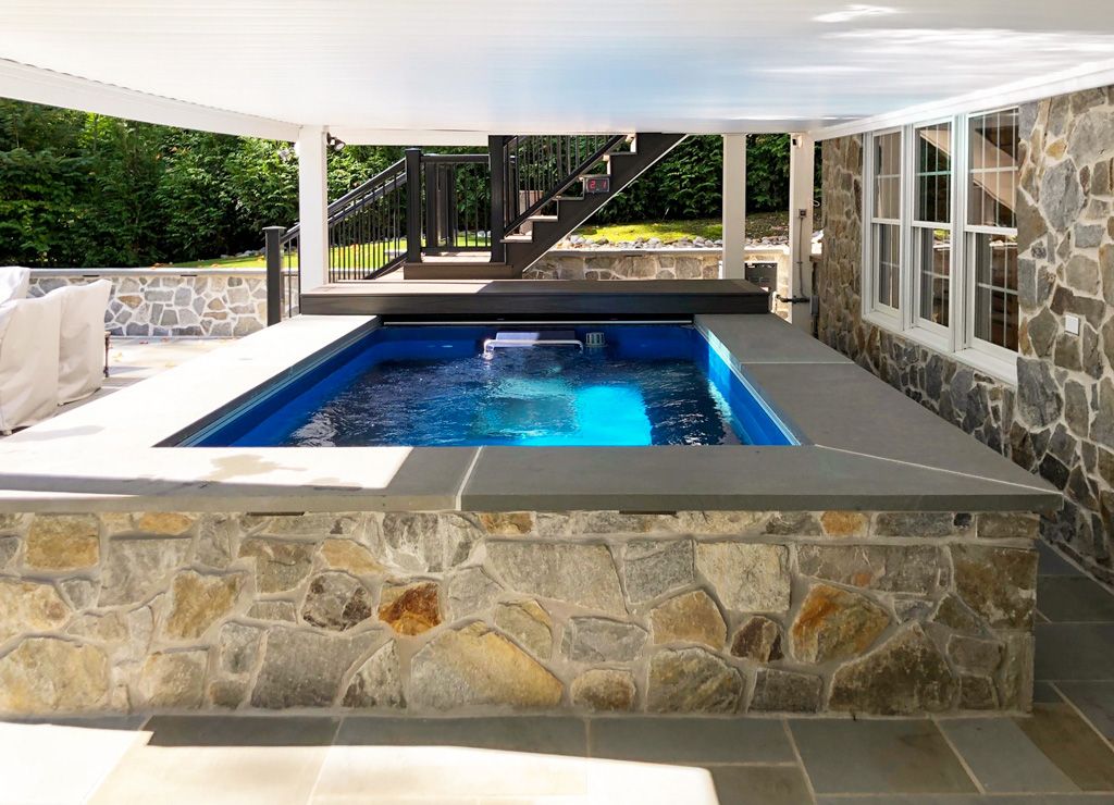 A picture of a stone, partially inground pool in a shaded area outdoors.