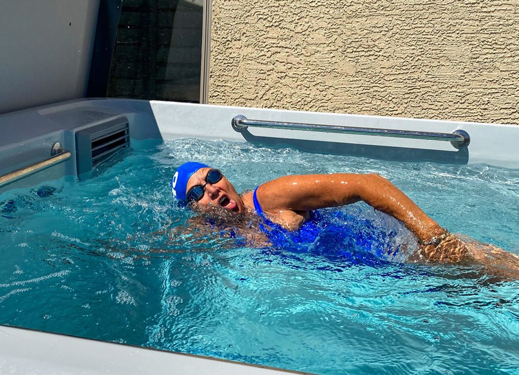 A picture of a woman in a blue swimsuit, cap, and goggles swimming against the current.