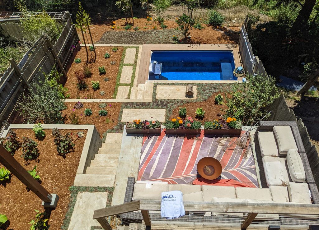 A picture of an entire backyard set-up, including a seating area around a fire pit, a pool, and a garden.