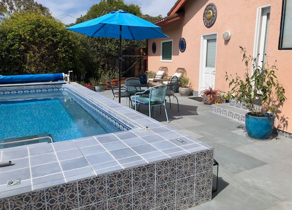 A picture of a tiled, aboveground pool with plants and outdoor furniture surrounding it.