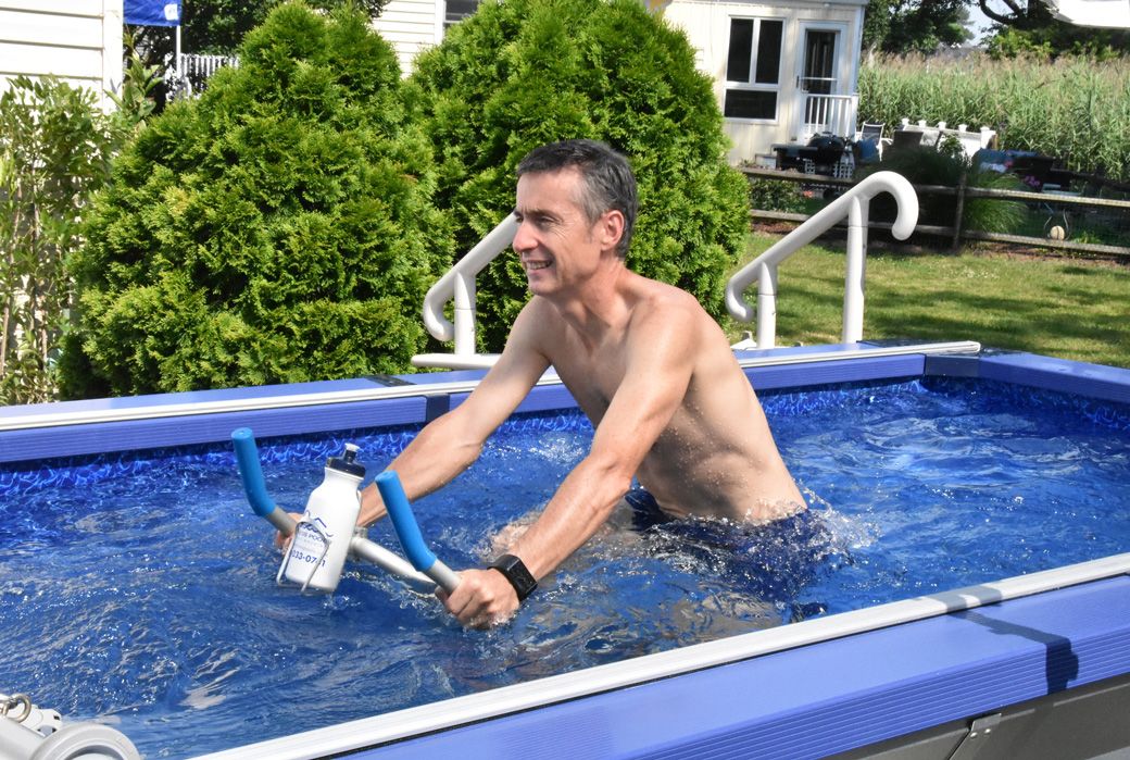 A picture of a man aqua cycling in an aboveground, backyard pool.