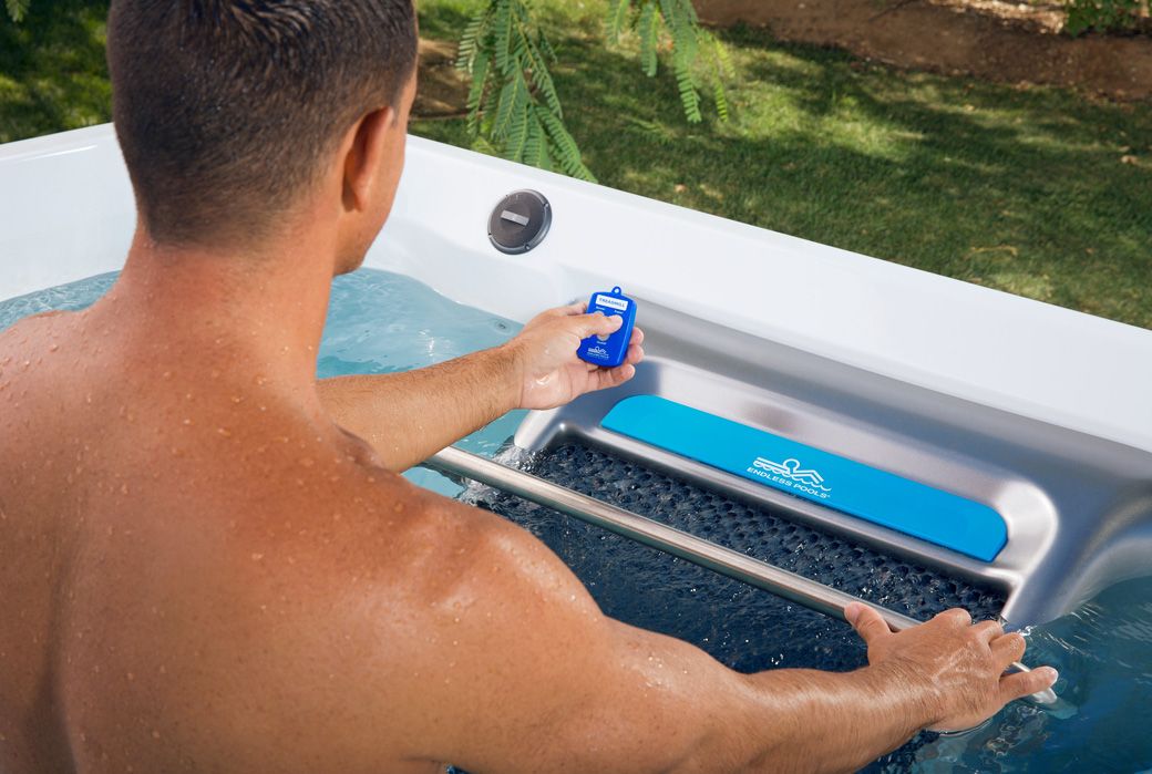 A picture of a man adjusting the settings of his water treadmill with a remote.