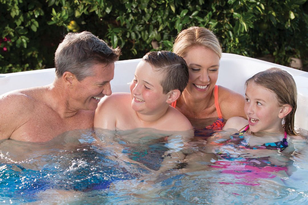 A picture of parents and their two kids all smiling at each other in one corner of their swim spa.