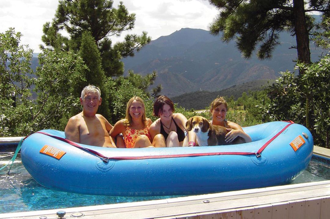 A picture of four people and their dog all sitting in a raft in their backyard pool.