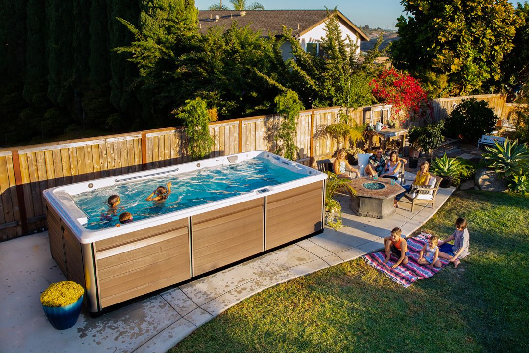 A picture of kids playing in an R-series swim spa while the adults sit talking at a table next to them.