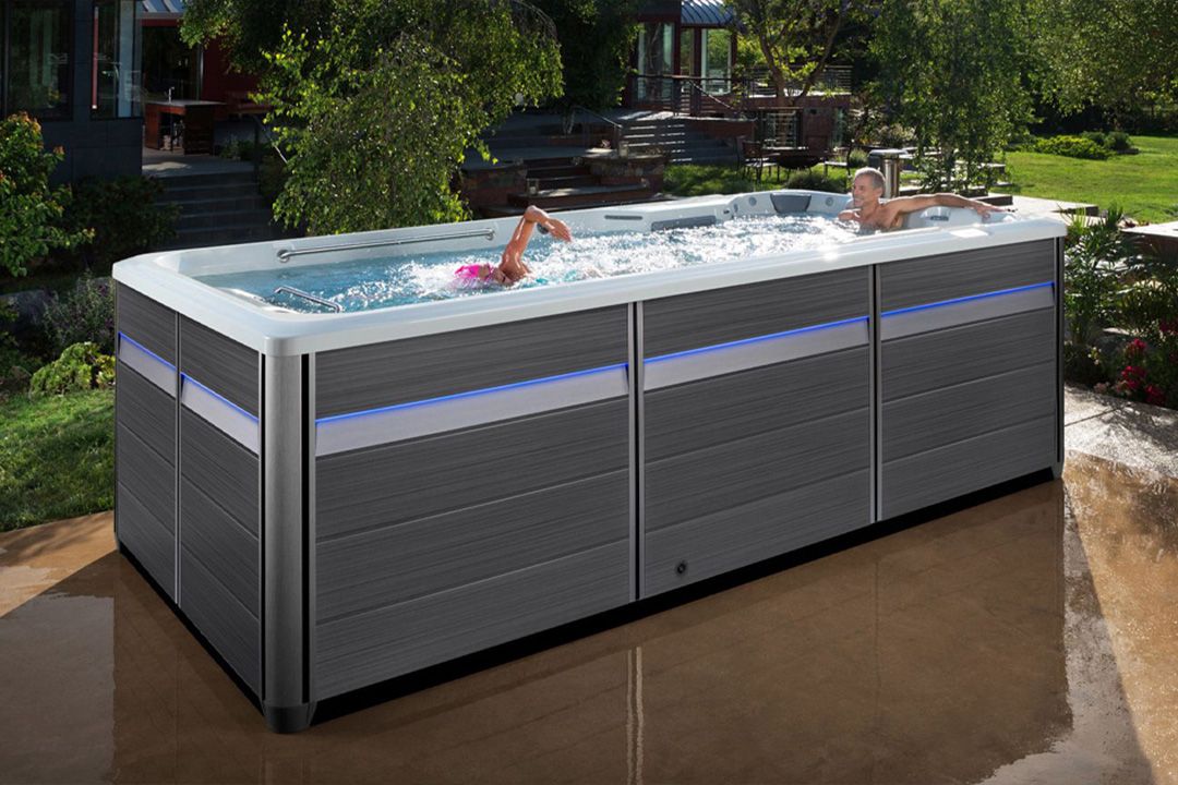 A fully above-ground swim spa installed on a patio in a beautiful backyard.