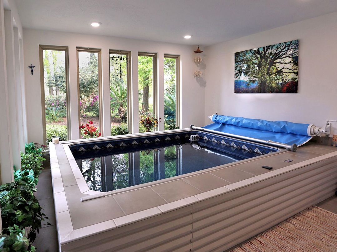 A picture of a sleek indoor pool set-up in a sunroom, with plenty of plants and windows for natural light.