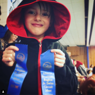 picture of a boy diagnosed with ADHD holds his swimming ribbons