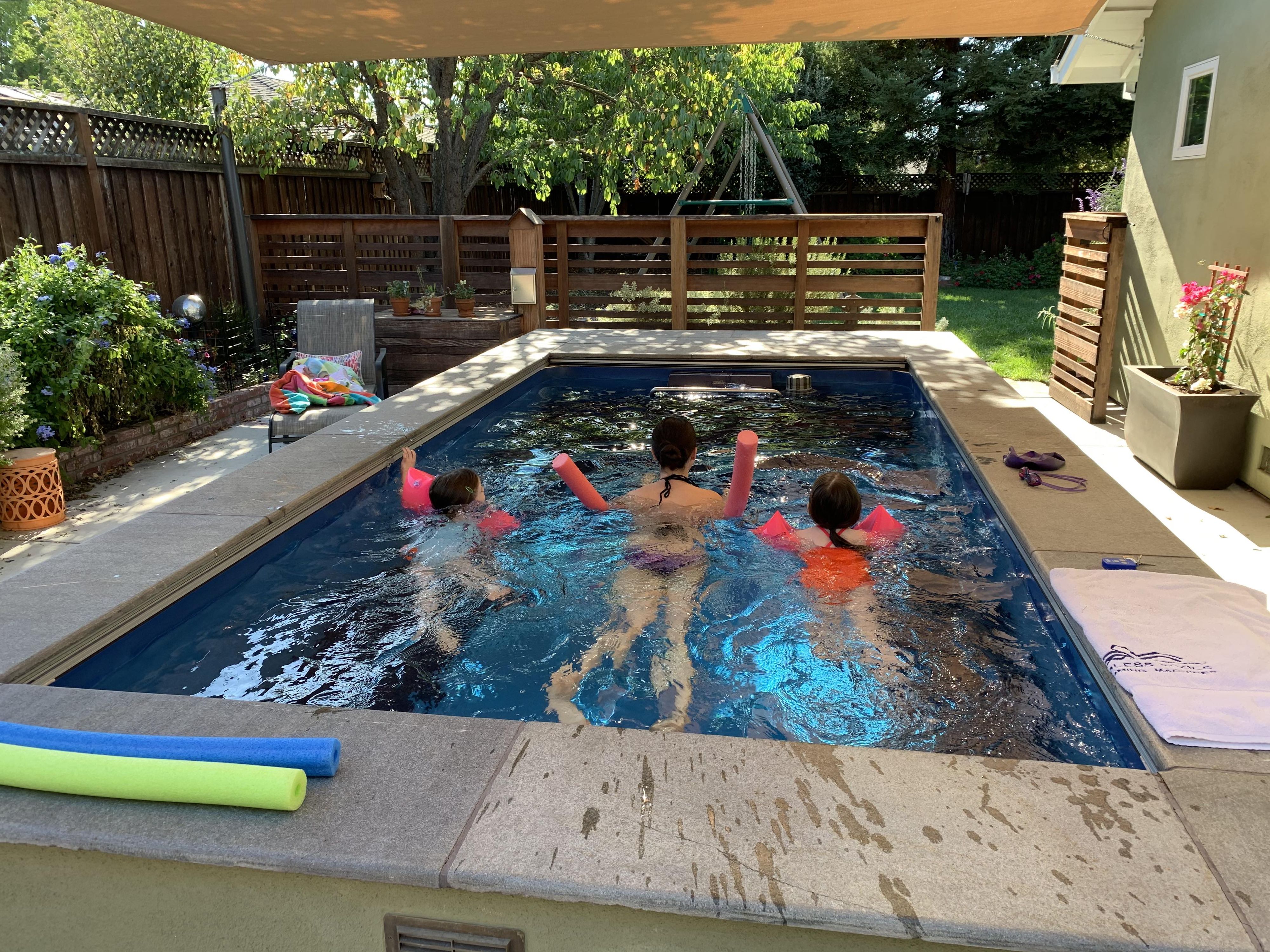 picture of mother and daughters with pool noodles in an Endless Pools backyard pool