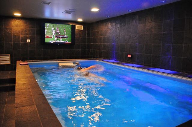 an indoor Endless Pools swimming machine in a black-tiled basement man cave