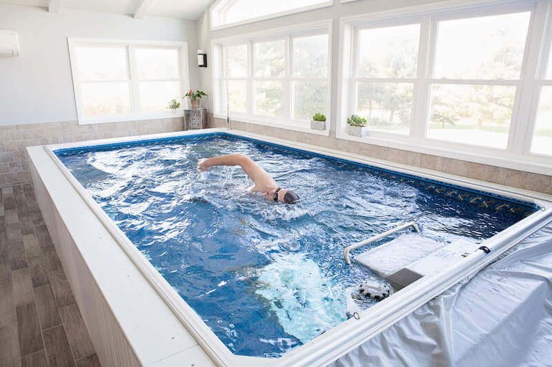 a swimmer swimming in a partially inground Original Endless Pool installed in a sunroom
