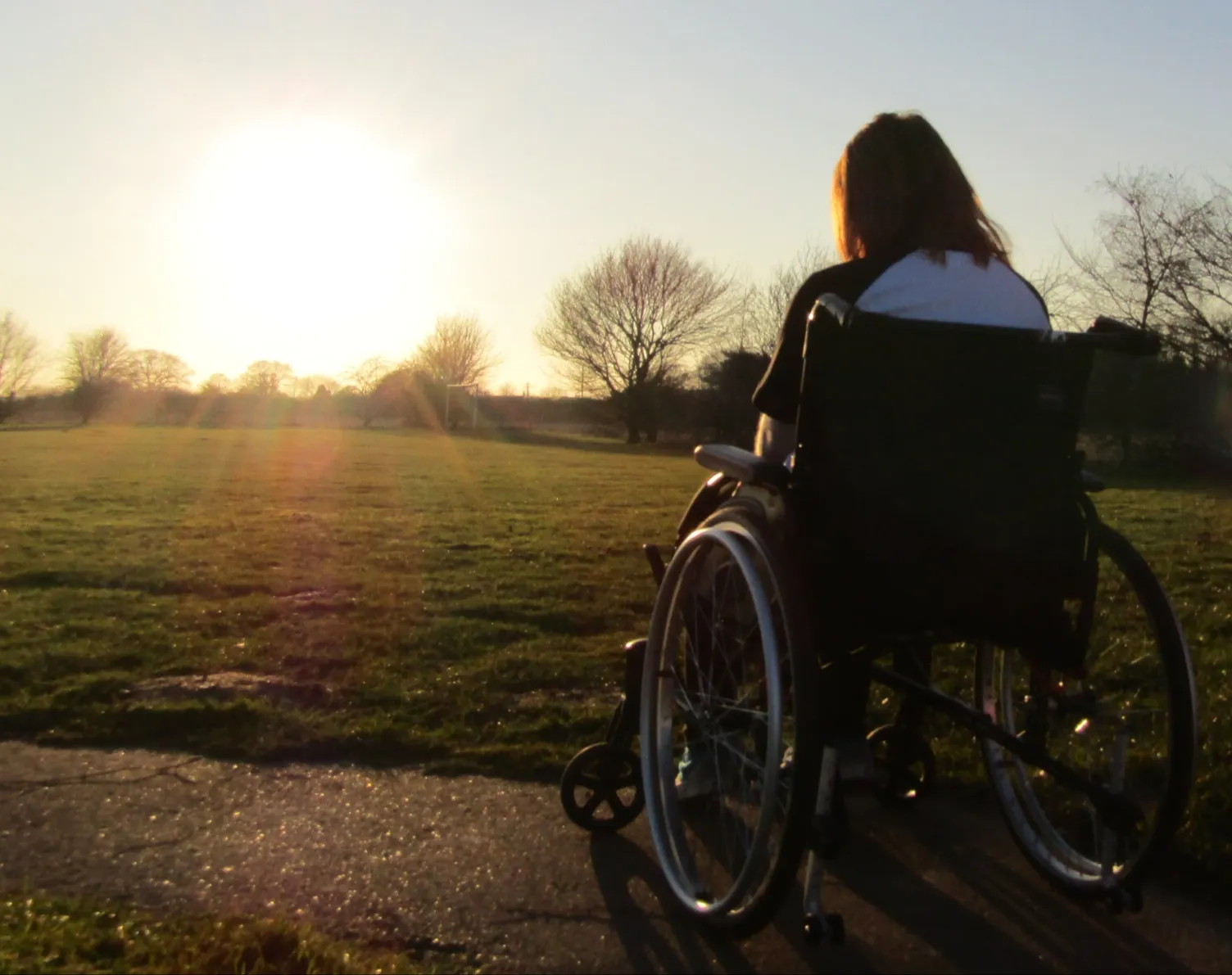 Woman sitting in a wheelchair with her back to the camera. The woman is watching the sunset in the distance.