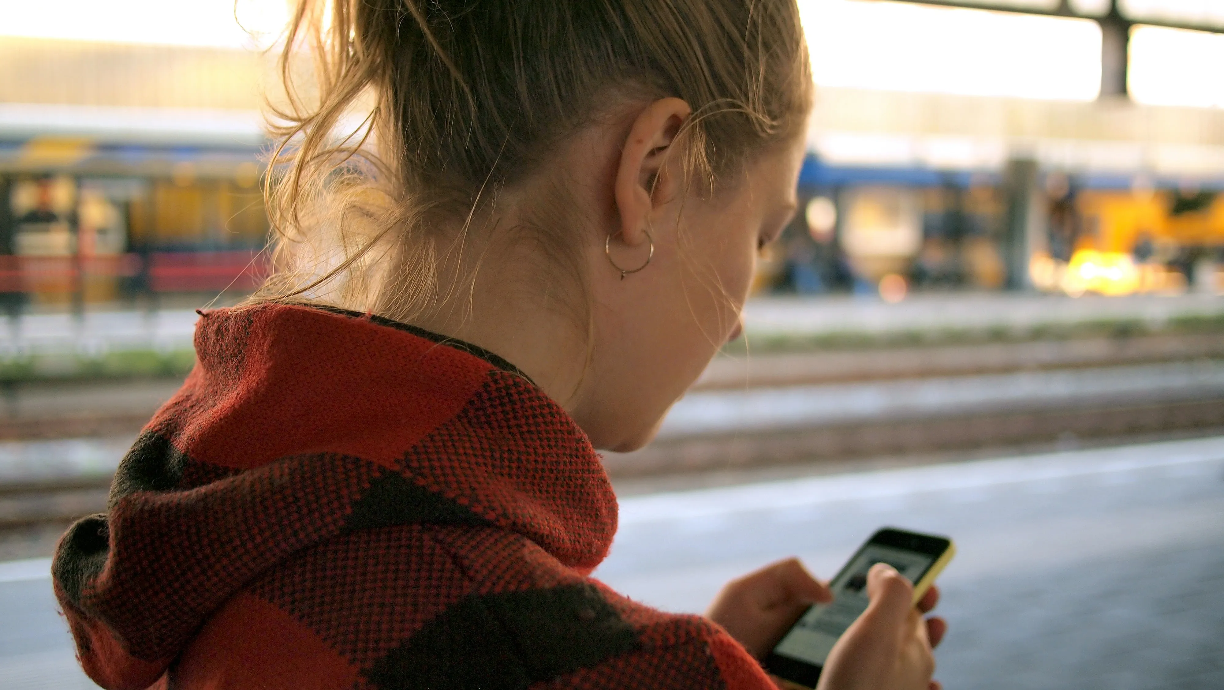 Getting started with screen readers: Woman using her phone, wearing a red jacket at a train station