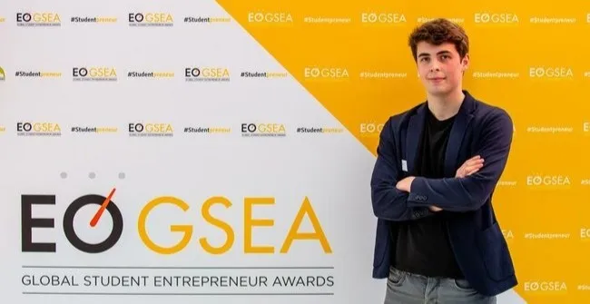 Freek standing in Front of a board with GSEA logo, wearing a Blue Jacket and having his hands folded.