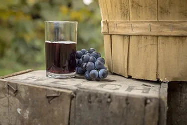 Close up of a glass of Welch's grape juice next to a basket of grapes