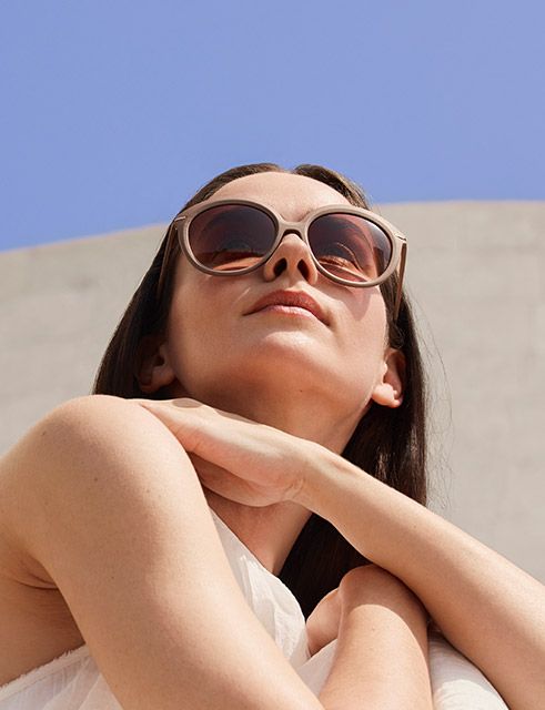 Occhiali da sole oversize con montatura scultorea color crema e lenti calde sfumate, presentati in una morbida composizione sovrapposta