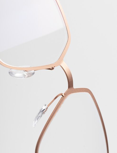 Close-up of Titanium Reframed eyeglasses featuring a laser-cut titanium full-rim frame with a flat sculpted profile and crisp architectural lines in a warm rose-gold finish.