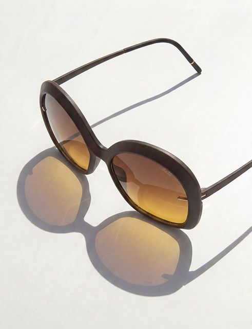 Oversized sunglasses with a sculptural brown-colored frame on a reflecting surface