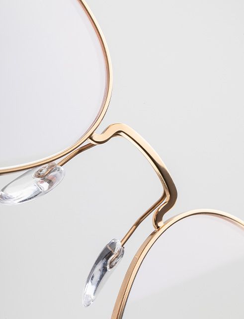 Close-up detail of the Pure Visionary eyeglasses showing the ultra-thin titanium profile wire frame, sculpted bridge, and transparent nose pads in a refined gold finish.