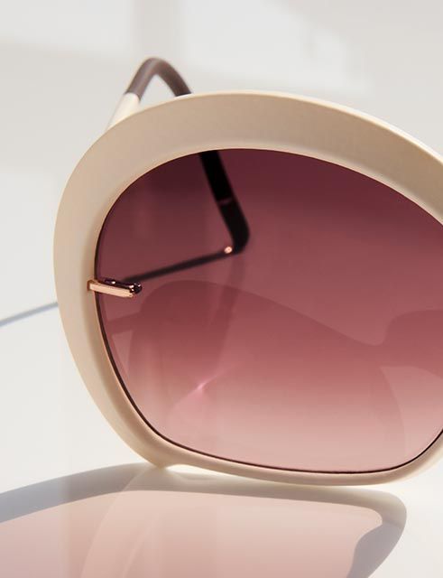 Primo piano di occhiali da sole oversize con montatura liscia color crema e lenti calde sfumate, che evidenziano dettagli raffinati, curve morbide e un design leggero e scolpito