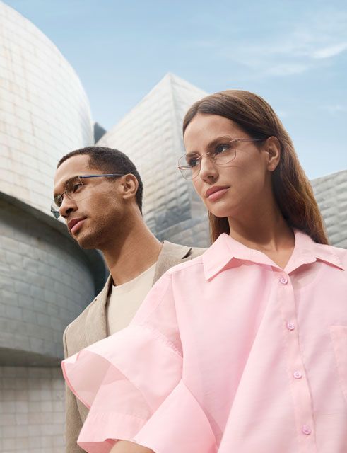 Portrait of a woman wearing Pure Visionary titanium eyeglasses with an ultra-thin profile wire frame, standing outdoors in front of the Guggenheim Bilbao Museum.