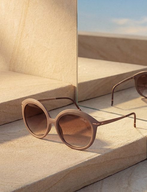 Occhiali da sole oversize con montatura marrone dal design scultoreo su una superficie riflettente