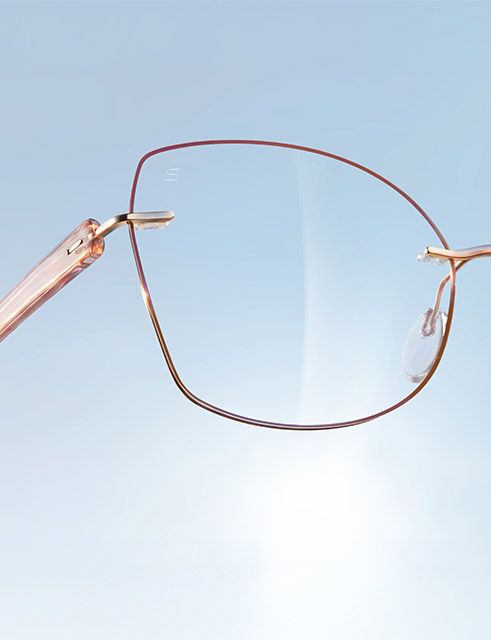 Portrait of a woman wearing Pure Visionary titanium eyeglasses with an ultra-thin gold profile wire frame, standing outdoors in front of the Guggenheim Bilbao Museum.